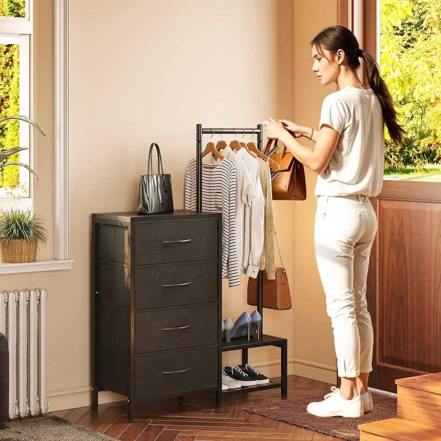 A woman stands beside a dark gray 4-drawer storage cabinet in a bright room, with a clothing rack, bags, and shoes nearby.