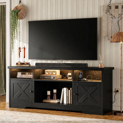 A black wooden TV stand/media console with two cabinet doors, open shelving, and a soundbar, shown in a styled living room setting with a large black television mounted above it.